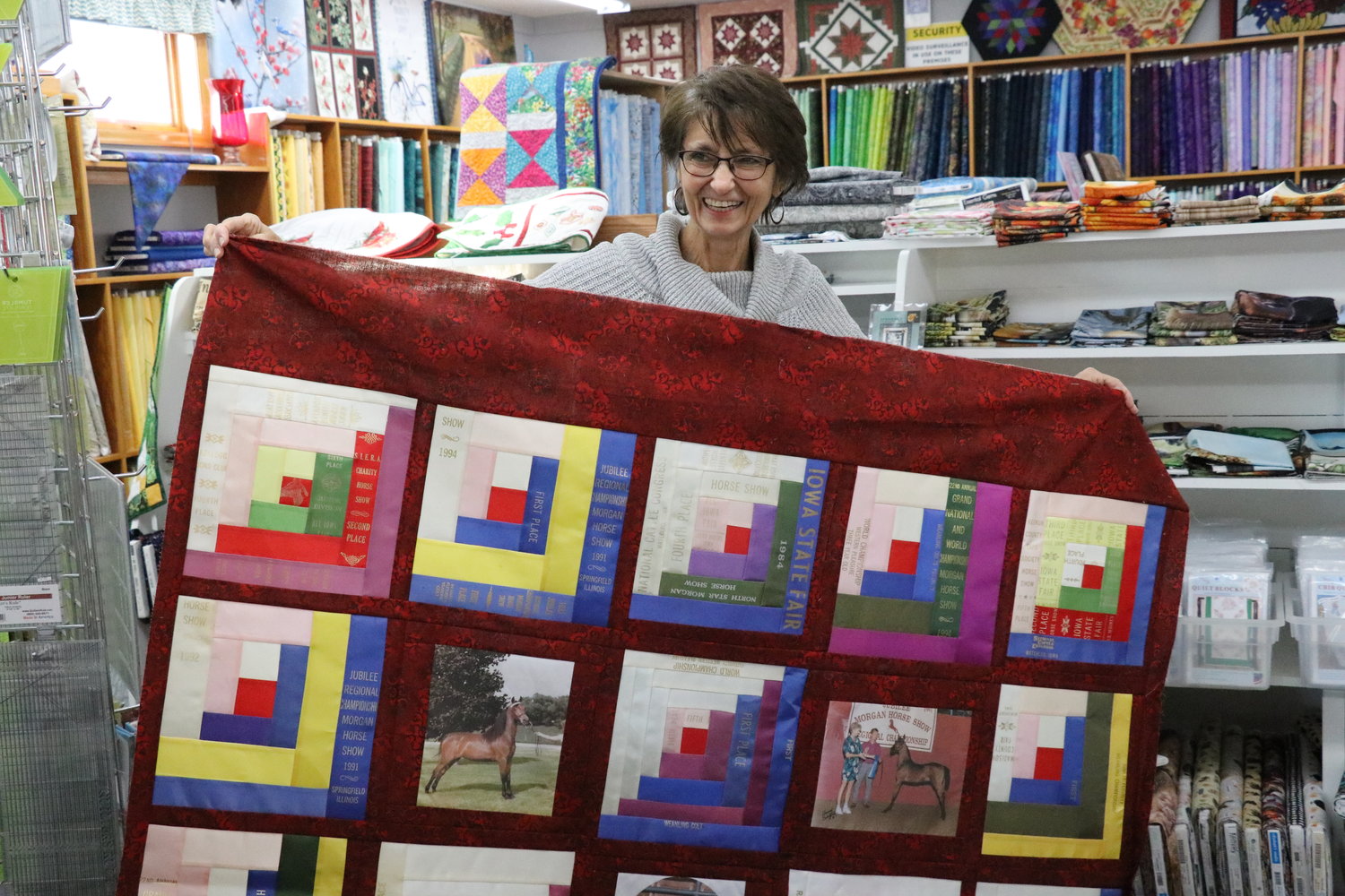 Grace Schumann shows off a quilt she made for a customer with horse show ribbons.